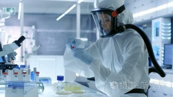 医学病毒学研究科学家从事危险品西装戴着面具，她用微管吸吮。她在一个无菌高科技实验室，研究设施工作