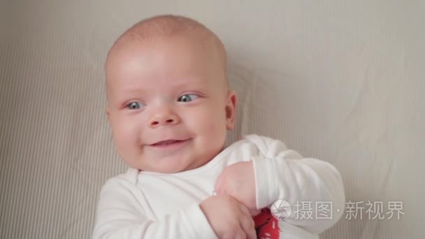 一个可爱的小婴儿望着镜头和快乐在白色的床单上
