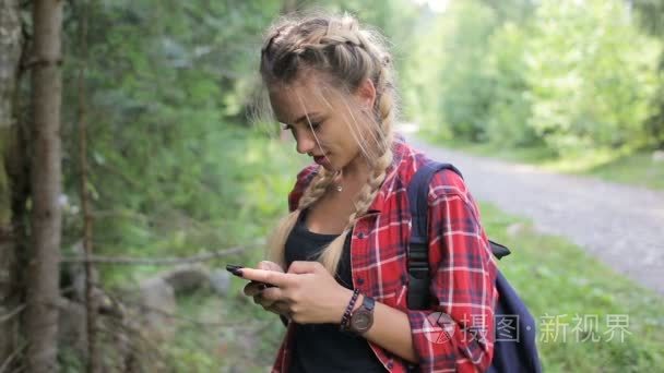 快乐的女孩站在智能手机上的森林和发短信的短信