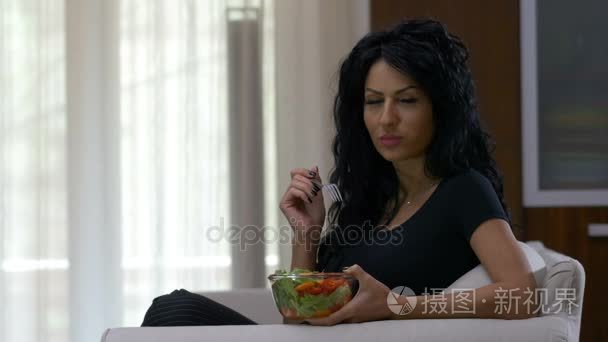 坐在沙发上在家里的健康低卡路里饮食生活方式的年轻女性善于吃蔬菜沙拉
