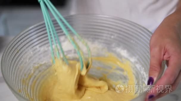 女性手准备面团混合成分在厨房里用打蛋器的特写视图。自制食品。慢动作镜头