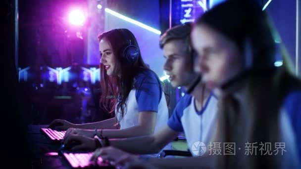 团队的专业电子竞技玩家玩网络游戏锦标赛竞争视频游戏中。女孩和男孩有耳机上，舞台上亮起霓虹灯