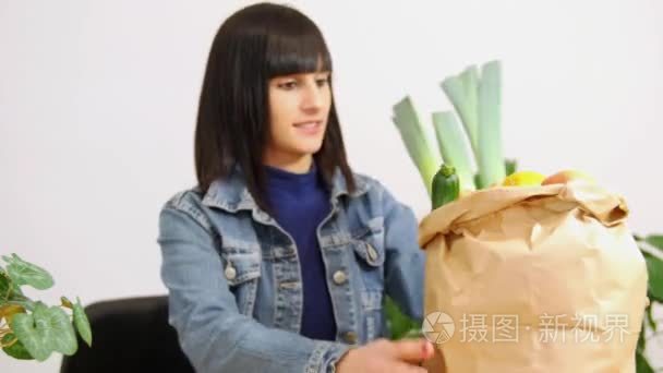 年轻的黑发女人，带着购物袋的蔬菜全吃一个苹果
