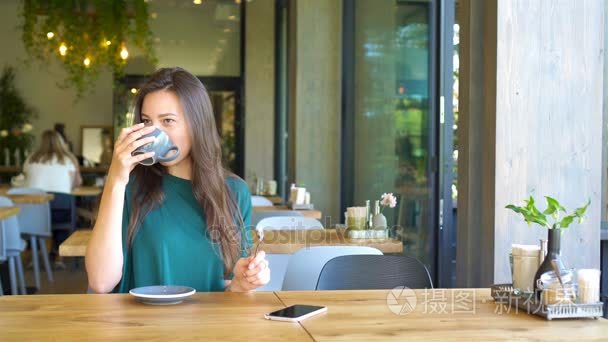 年轻女人独自坐在咖啡厅在空闲时间进行细胞电话呼叫。有吸引力的女性，可爱的笑容，有说用手机在咖啡馆里其余的谈话视频