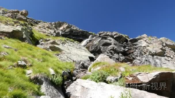 夏季在田园诗般的无污染的环境跨越绿色草地和阿尔卑斯山巨石流动的瀑布。慢动作放大