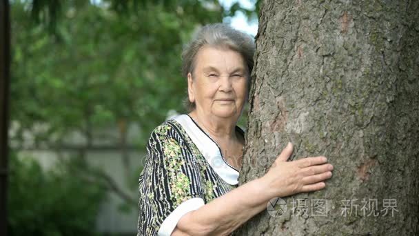 老年妇女抱着相机的树微笑视频