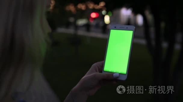 在晚上女人抱着一个绿色的屏幕智能手机