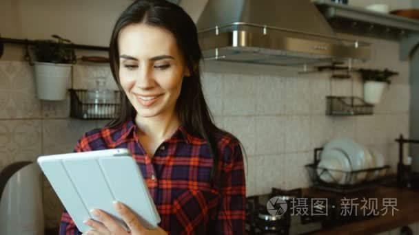 年轻漂亮的女人在厨房里使用平板电脑而站。上网，阅读食谱的女人。关闭