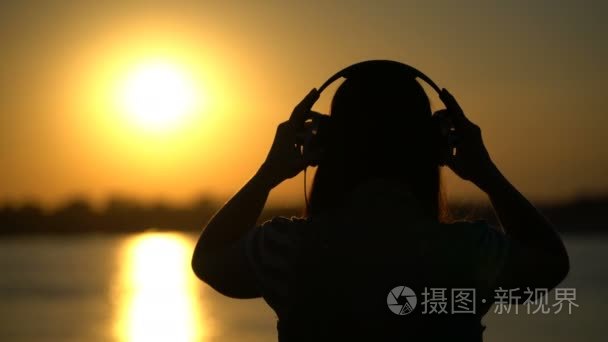 女人听着耳机上日落背景音乐视频