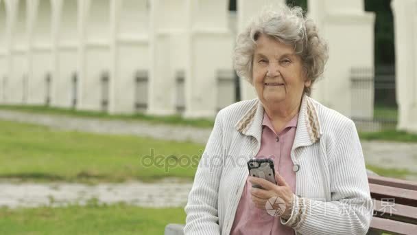 老年妇女抱着银的智能手机在户外视频