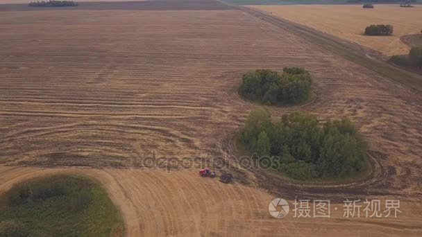 耕地的田野上空的无人机空中： 射击。红色的拖拉机清除字段在秋天