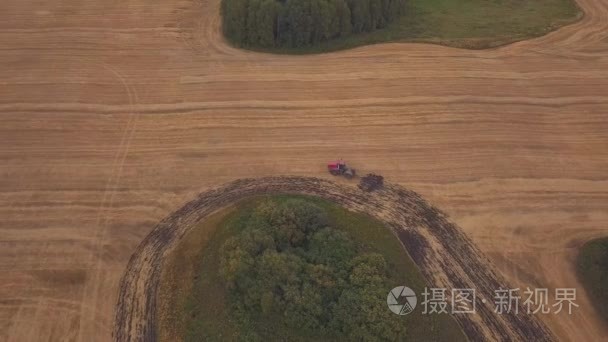 耕地的田野上空的无人机空中： 射击。红色的拖拉机清除字段在秋天