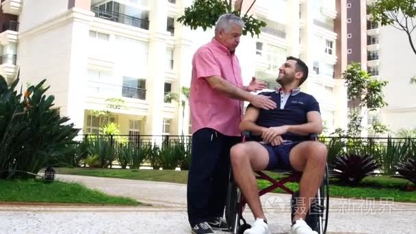 父亲鼓励他残疾的儿子在轮椅在公园