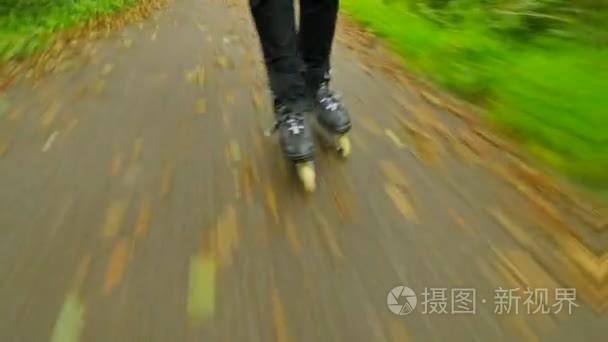 在湿滑沥青在秋季森林的室外轮滑。男子双腿在黑色运动长裤。快速运动的内联靴子路上满了树叶秋天 ccolorful