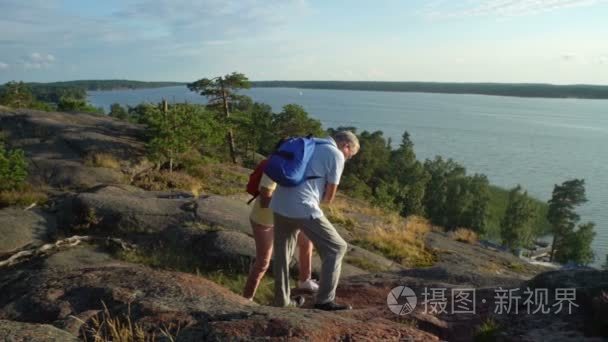 积极对老年夫妇在岩石上攀爬和欣赏日出，日落视频