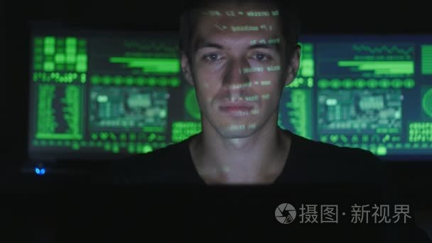 黑客程序员在计算机上工作，而绿色代码字符反映在他的脸在黑暗的办公室