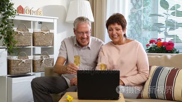 老年夫妇与朋友用笔记本电脑打电话给摄像机和喝香槟