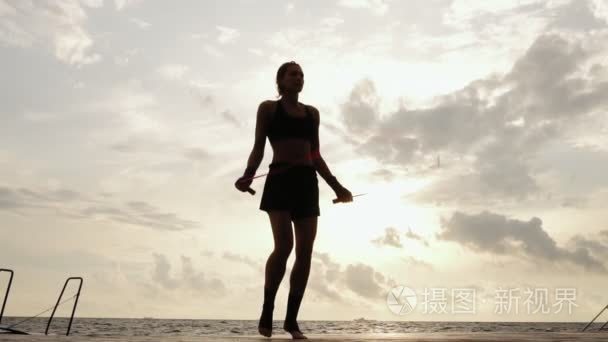 无法辨认运动女人锻炼跳绳对着太阳的慢动作的海滩。跳上一根跳绳在海边的女孩