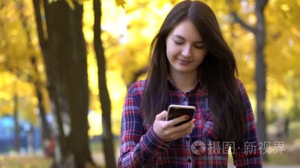 女孩在秋天在公园散步，和她的智能手机使用的应用程序