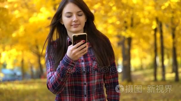 女孩在秋天在公园散步，和她的智能手机使用的应用程序
