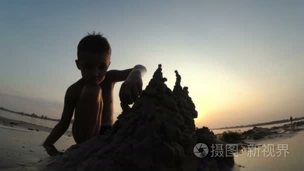 一个孩子上海滩沙子城堡在日落时分的轮廓