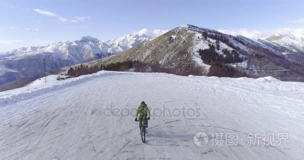 在骑自行车的人的结核分枝杆菌的 e 自行车冬季下雪路上骑车人的落后天线。在户外在冬天的雪地上骑自行车。4 k 飞行视频