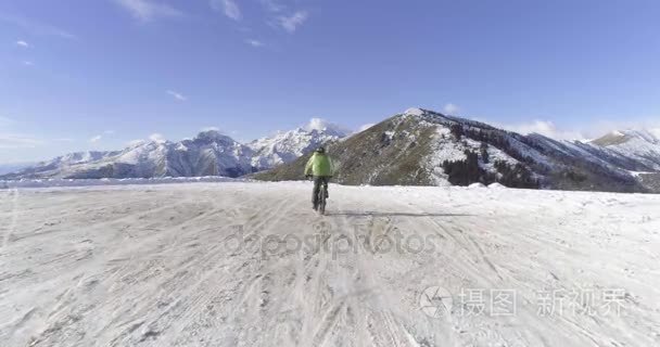 在骑自行车的人的结核分枝杆菌的 e 自行车冬季下雪路上骑车人的正向空中。在户外在冬天的雪地上骑自行车。4 k 无人机飞行视频