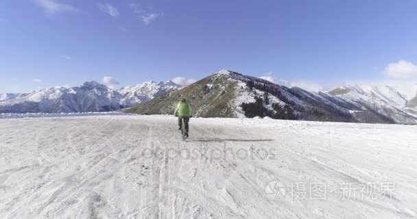 在骑自行车的人的结核分枝杆菌的 e 自行车冬季下雪路上骑车人的正向空中。在户外在冬天的雪地上骑自行车。4 k 无人机飞行视频