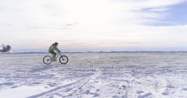 骑自行车的人的结核分枝杆菌的 e 自行车冬季下雪路上骑车人在空中一侧。在户外在冬天的雪地上骑自行车。4 k 无人机飞行视频