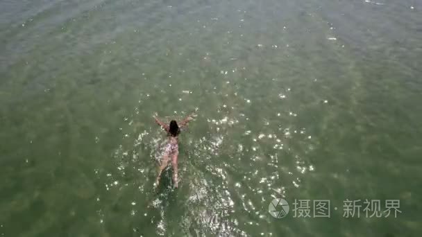 夏季蓝色海浪中游泳的细长女孩的空中拍摄