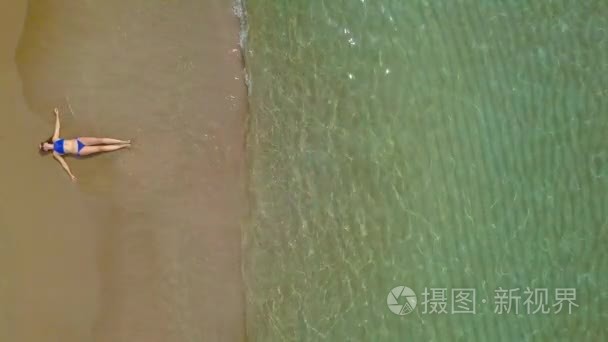空中射击的女人穿着比基尼躺在沙滩和海浪洗她的脚