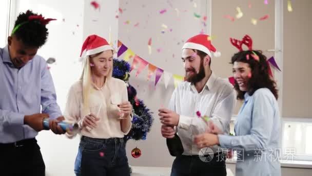 年轻的人庆祝圣诞节和新年在办公室用五彩纸屑打开一瓶起泡酒和哑炮爆炸药包组。慢动作镜头