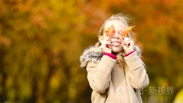 可爱的小女孩，在户外在美丽温暖一天用黄色的叶子在秋天的肖像