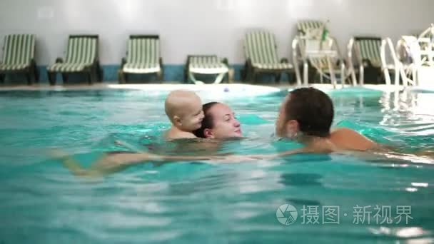 在游泳池里和他可爱的小孩的年轻家庭。那个男孩游泳在他母亲的背上。幸福的家庭，池中的乐趣