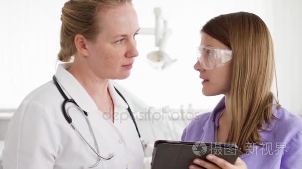 两名女医生用平板电脑在病房讨论新的治疗方法。持有瓶丸