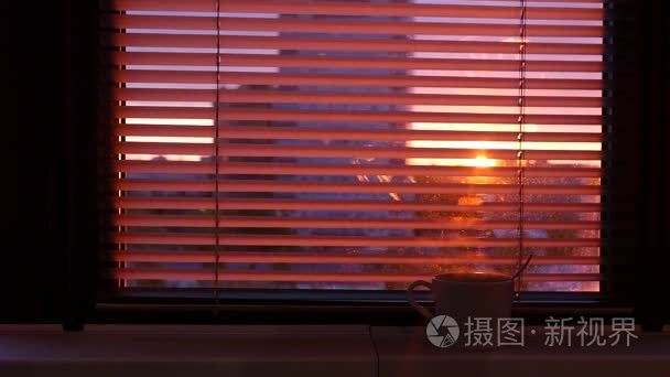 窗台上有一杯热茶或咖啡  在封闭的百叶  你可以看到城市和日落的光线。slowmotion.1920x1080