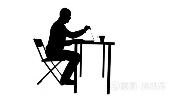 男人坐在桌子旁喝咖啡, 用笔记本电脑的剪影短视频