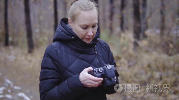 手里拿着相机的女孩摄影师看了照照片。秋天的森林  第一场雪。电影拍摄  慢镜头拍摄