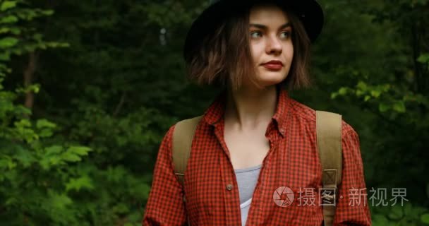 旅游的年轻女子戴着帽子走在山上。活跃的健康的时髦女孩在森林里徒步旅行  背着背包走在山上的小路上