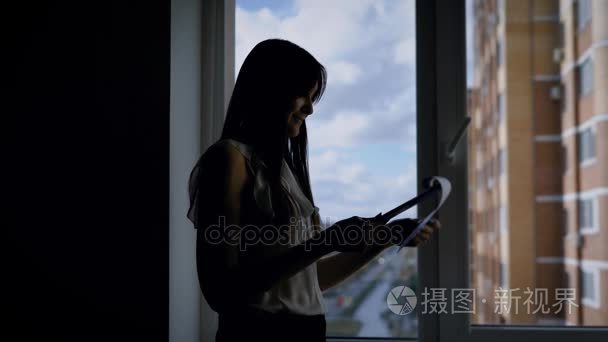 开朗的女人在她公司的办公室里学习协议  站在靠近窗口的城市景观