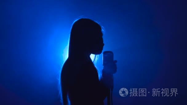 女孩在唱歌的复古麦克风欢闹的歌曲。烟雾背景。剪影.侧面视图