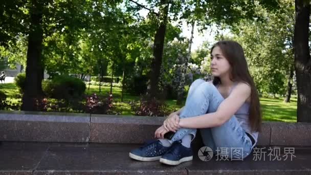 可爱的十几岁的女孩检查电话和等待的电话  坐在公园。视频素材高清拍摄静态相机