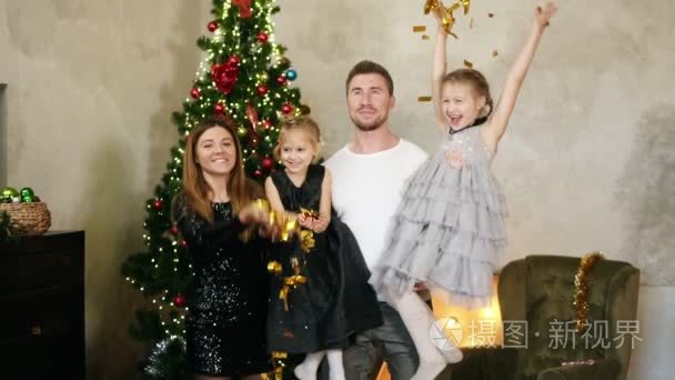 Slowmotion 拍摄的年轻幸福的家庭四的圣诞树上扔了金色的五彩纸屑。可爱的母亲  父亲和两个女儿一起庆祝圣诞节