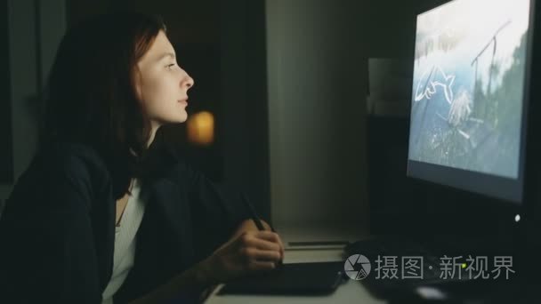 集中的年轻妇女设计师晚上工作在办公室用计算机和图表片剂完成工作