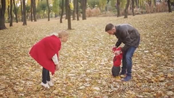 美丽的家庭在公园里享受着秋日的漫步。一个小孩子学着和父母一起散步  家长帮他迈出了第一步。