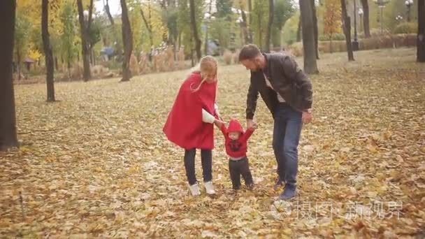 美丽的家庭在公园里享受着秋日的漫步。一个小孩子学着和父母一起散步  家长帮他迈出了第一步。