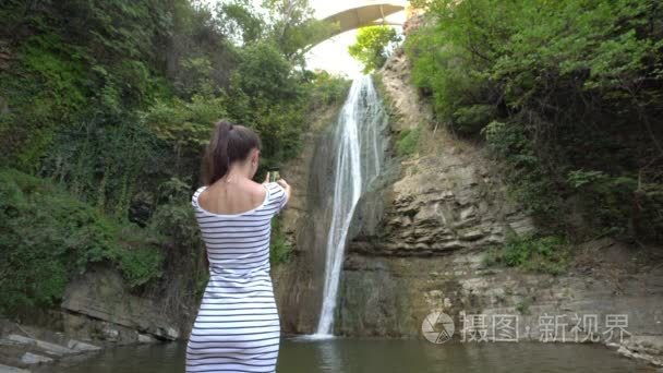 一位年轻的女士在拍瀑布的照片视频