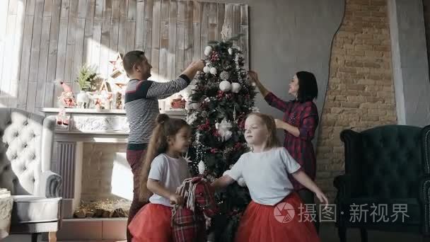 年轻的父母装饰着一棵圣诞树, 他们的双胞胎女儿骑着一匹玩具马。新年和圣诞节快乐