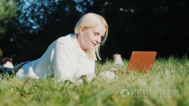 一个女人躺在草坪上  用笔记本电脑。下次奔跑在小狗附近