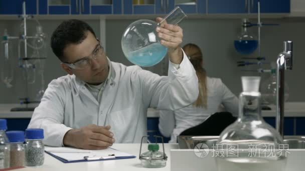 男性科学家在实验室里用液体检查烧瓶